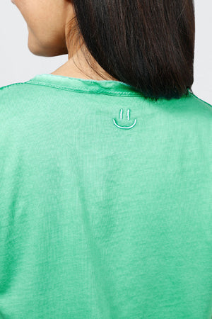Organic Rags Happy V Neck Tee in Apple Green. V neck short sleeve top with raw edge at banded neckline. Slightly faded wash. Smiley face embroidered at back neckline. Relaxed fit._34960620978376