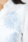 Elliott Lauren Embroider Me Shirt in White.  White pointed collar button down blouse with delicate sky blue floral and leaf embroidered motif on left side.  Long sleeve with button cuff.  Shirt tail high low hem with side inset.  Relaxed fit._t_60267567710574