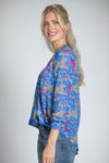 APNY Surplice Front Tassel Top. Blue and gray abstract camo print with pink accents. Banded crew neck with tassel ties. Surplice front with hidden snap. Gathered long sleeve with elastic cuff. High low hem. Relaxed fit._t_34808826200264