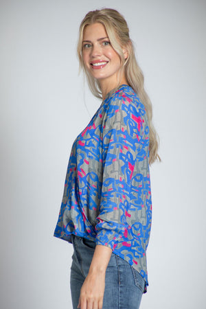 APNY Surplice Front Tassel Top. Blue and gray abstract camo print with pink accents. Banded crew neck with tassel ties. Surplice front with hidden snap. Gathered long sleeve with elastic cuff. High low hem. Relaxed fit._34808826200264