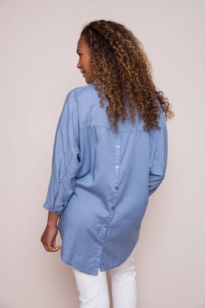 Suzy D Bonny Button Back Top in Jeans. Pointed collar split v shirt with center seam. Dolman 3/4 sleeve with button cuff. Soft side gathers. Back yoke with button detail down center back. High low hem. Slightly oversized fit._34225143349448