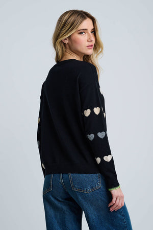 Lisa Todd Love Tracks Sweater in Black with 1 row each of white, beige and gray intarsia hearts.  Cotton/cashmere pullover crew neck sweater.  Long sleeves with dropped shoulders.  Intarsia hearts in front and sleeves.  Plain back.  Blanket stitch trim at cuffs. Rib trim at neck hem and cuff.  Classic fit._61429886189934