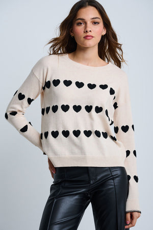 Lisa Todd Love Tracks Sweater in Sheepskin with black intarsia hearts.  Cotton/cashmere pullover crew neck sweater.  Long sleeves with dropped shoulders.  Intarsia hearts in front and sleeves.  Plain back.  Blanket stitch trim at cuffs. Rib trim at neck hem and cuff.  Classic fit._61429884551534