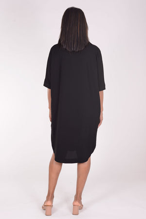 Perlavera Dina Dress in Black. Below the knee popover dress with pointed spread collar, hidden button placket and short cuffed sleeves. Curved high low hem. In seam pockets. One size fits most._34324036059336