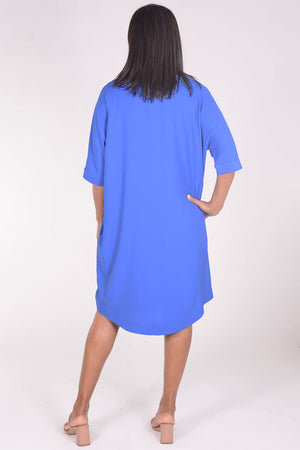Perlavera Dina Dress in Blue. Below the knee popover dress with pointed spread collar, hidden button placket and short cuffed sleeves. Curved high low hem. In seam pockets. One size fits most._34324035961032