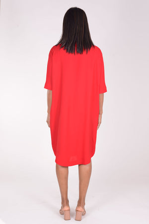 Perlavera Dina Dress in Red. Below the knee popover dress with pointed spread collar, hidden button placket and short cuffed sleeves. Curved high low hem. In seam pockets. One size fits most._34324035993800