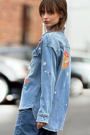 Billy T Festival Denim Shirt in Denim. Classic denim mid weight shirt with bright multi colored embroidered appliques. Pointed collar button down with 2 front button flap patch pockets. Long sleeve with button cuff and roll button tab. High low shirt tail hem. Relaxed fit._34304929857736